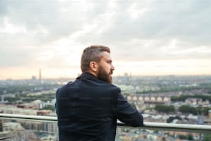 Uma visão traseira do empresário hipster de pé contra o panorama da vista de Londres.