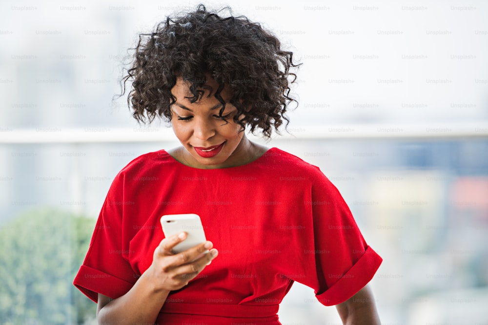 Um retrato em close-up de mulher negra em vestido vermelho com smartphone, mensagens de texto.