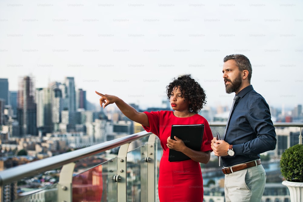 A portrait of businesspeople standing against London rooftop view, pointing to something and talking.