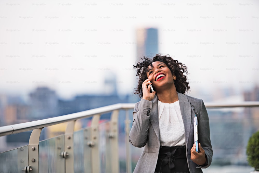 A portrait of black businesswoman standing on a terrace against London rooftop view panorama, making a phone call. Copy space.