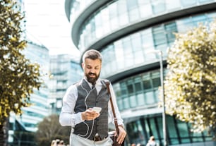 Hipster businessman with smartphone and earphones walking on the street in London, listening to music.