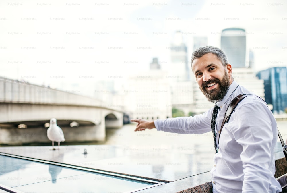 A hipster businessman standing by the river in London, pointing at seagull.
