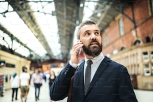 ロンドンのトライアン駅でスマートフォンを持つ幸せなビジネスマンが電話をかける。