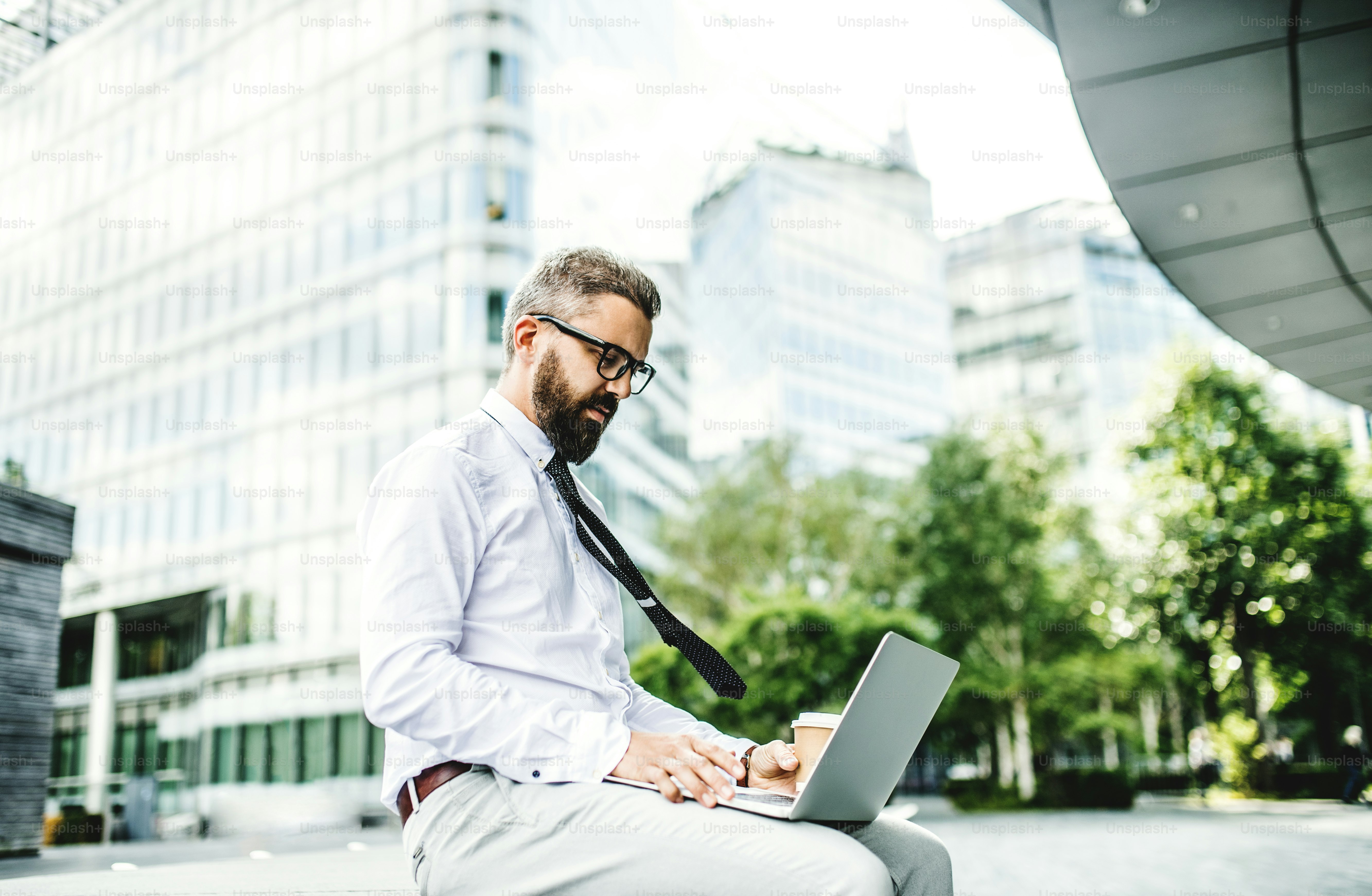 Hombre de negocios hipster con computadora portátil sentado al aire libre en la calle de la ciudad.