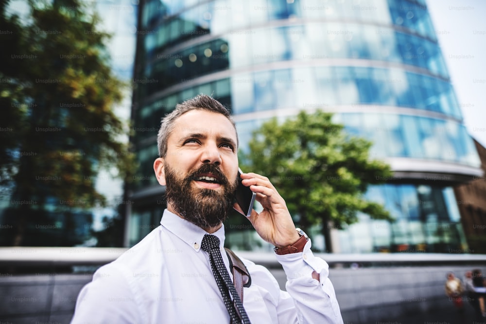 Un primer plano de un hombre de negocios hipster con un teléfono inteligente en la ciudad, haciendo una llamada telefónica. Espacio de copia.