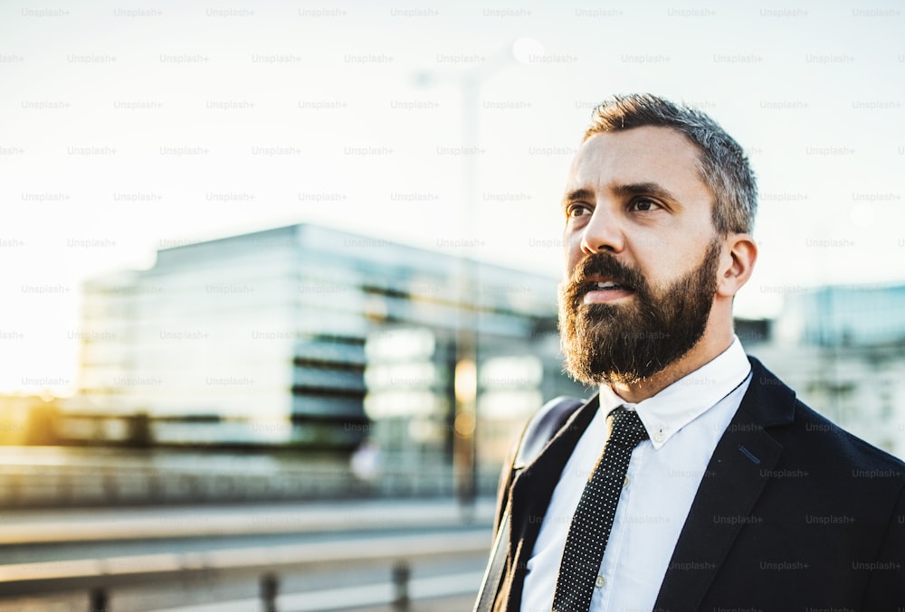 Hipster businessman walking on the street in the city at sunset. Copy space.