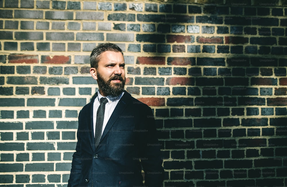 Hipster businessman standing against brick wall on the street in London. Copy space.