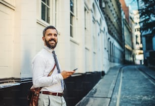 Hipster businessman standing on the street in London, holding smartphone. Copy space.