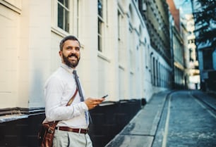 Uomo d'affari hipster in piedi per strada a Londra, con in mano lo smartphone. Copia spazio.