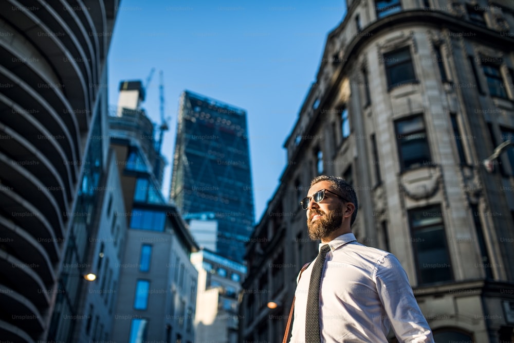 Vista de baixo ângulo de empresário hipster com óculos escuros em pé na rua na cidade de Londres. Espaço de cópia.
