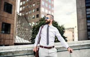 Hipster businessman with sunglasses, suitcase and laptop bag standing on the street in London.