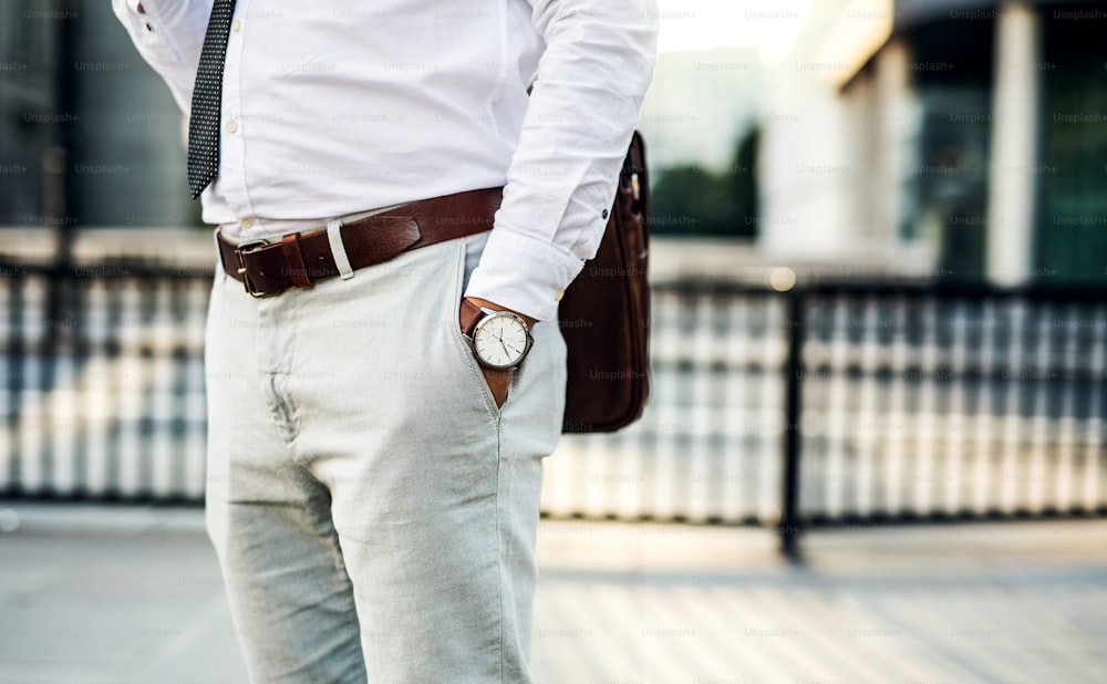 Homme d’affaires méconnaissable avec une montre debout dans la rue en ville, la main dans les poches.