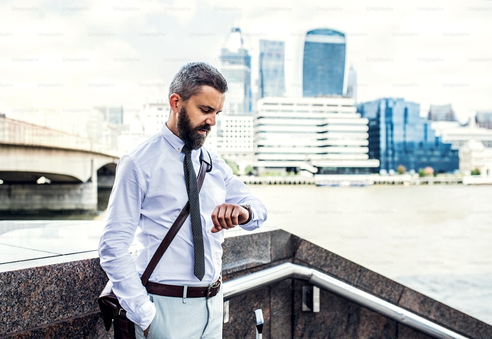 Uomo d'affari hipster in piedi vicino al Tamigi a Londra, controllando l'ora. Copia spazio.