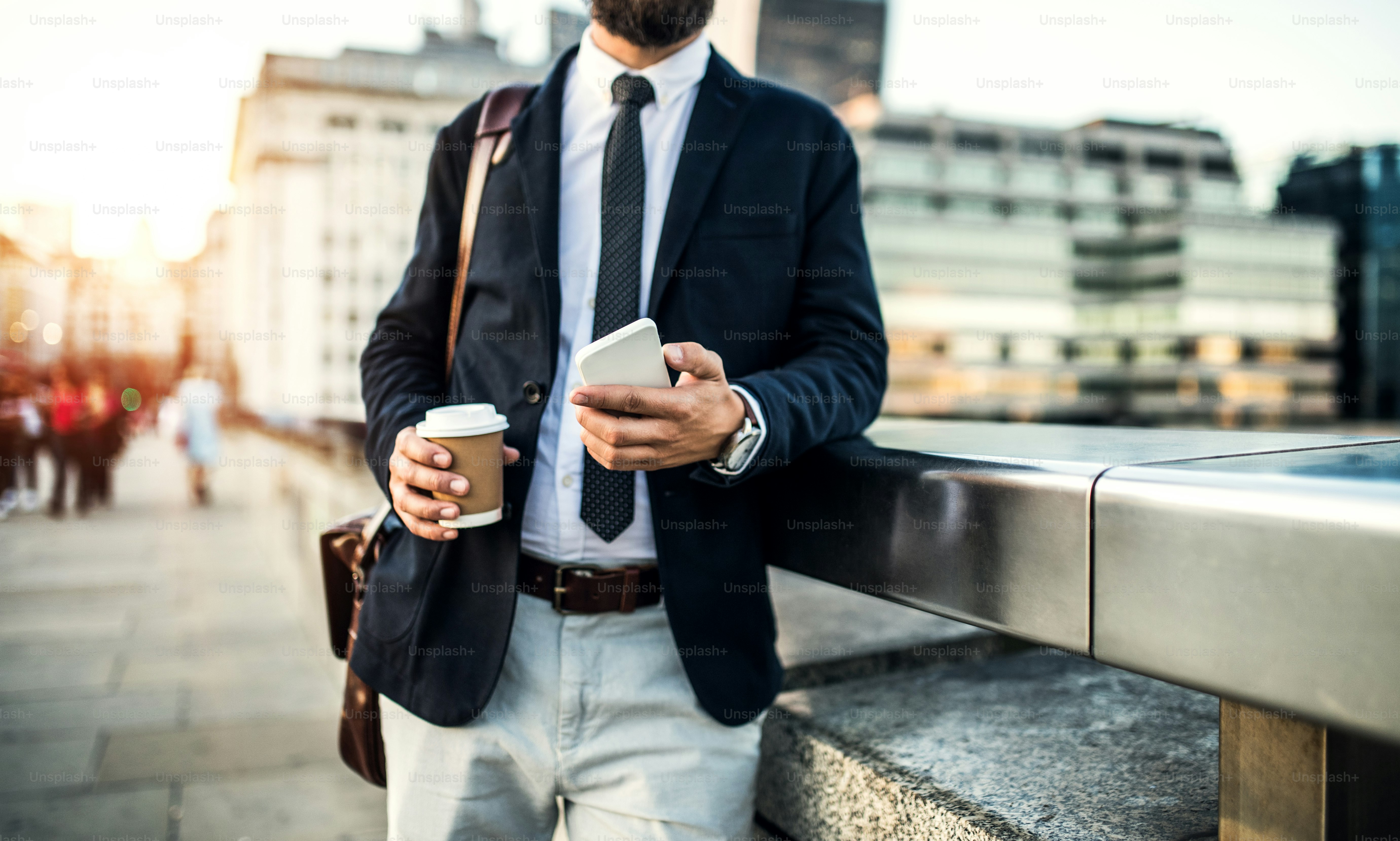 Pengusaha yang tidak dikenali dengan smartphone dan kopi berdiri di jembatan di London.