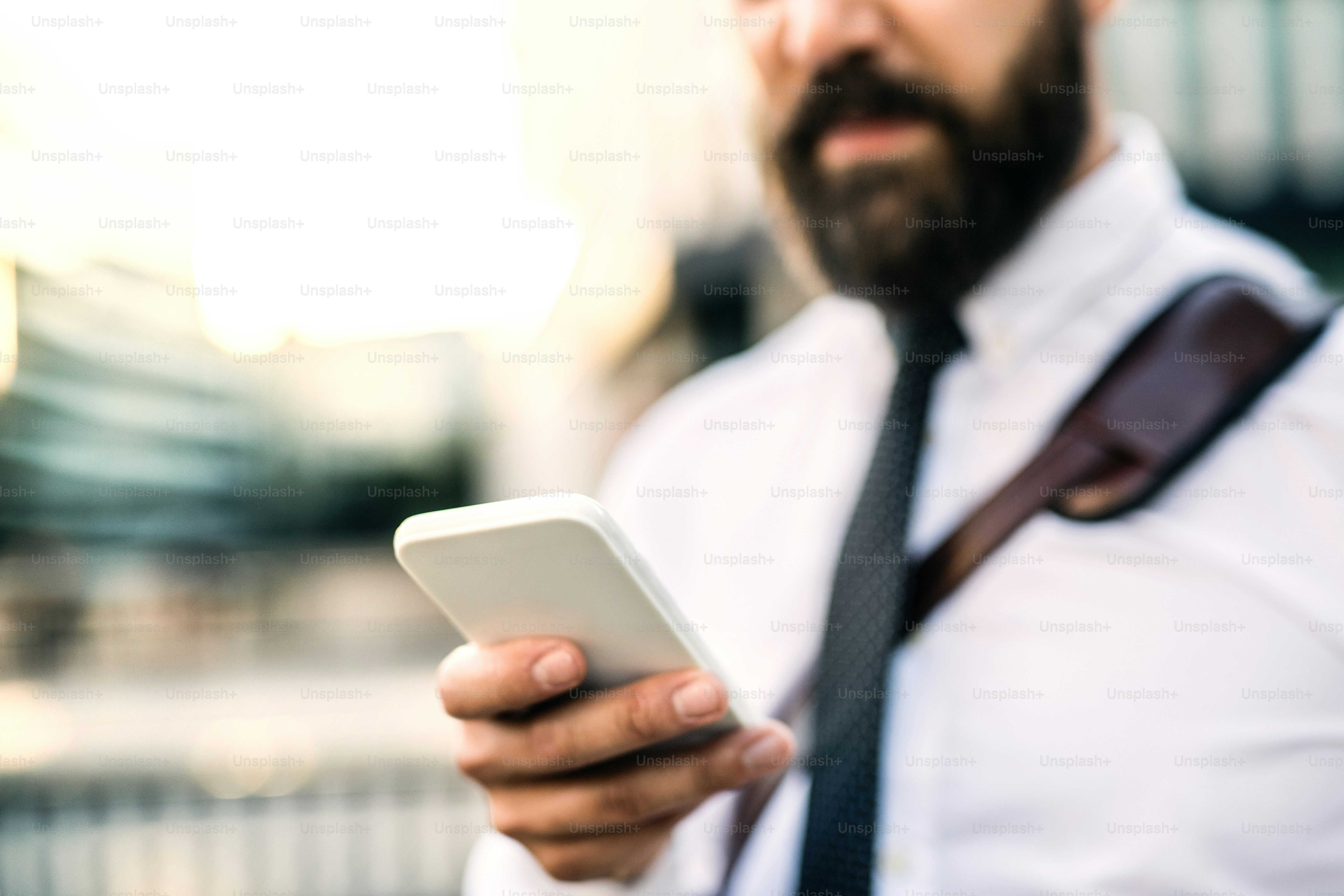 Hombre de negocios irreconocible con teléfono inteligente parado en la calle en la ciudad, mensajes de texto.