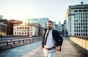Uomo d'affari hipster che corre per strada in città al tramonto.