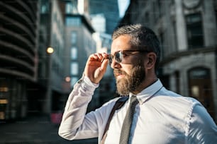 Hombre de negocios hipster con gafas de sol parado en la calle en la ciudad de Londres. Espacio de copia.