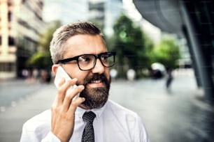 Un primer plano de un hombre de negocios hipster con un teléfono inteligente en la ciudad, haciendo una llamada telefónica. Espacio de copia.