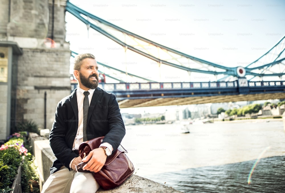 ロンドンのタワーブリッジのそばに座っているバッグを持つ流行に敏感なビジネスマン。スペースをコピーします。