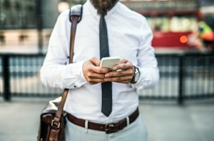 Unrecognizable businessman with smartphone standing on the street in city, text messaging.