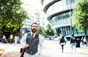 Hipster businessman with a bag and earphones walking on the street in London.
