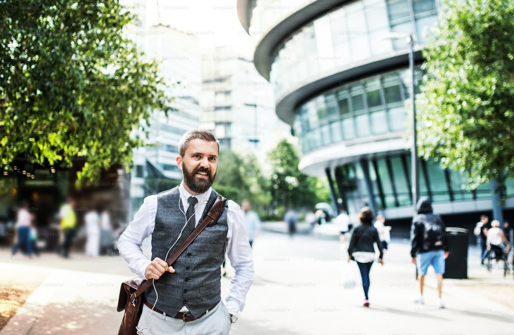 Hipster businessman with a bag and earphones walking on the street in London.