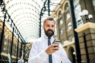 Uomo d'affari felice con smartphone sulla stazione trian di Londra, messaggi di testo.