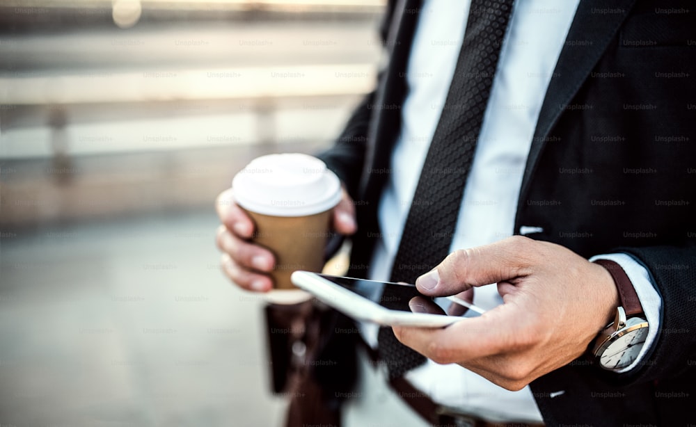 Eine Nahaufnahme eines nicht wiederzuerkennenden Geschäftsmannes mit Smartphone und Kaffee in einem Pappbecher in der Stadt, SMS. Speicherplatz kopieren.