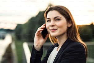 Um close-up de uma jovem empresária com smartphone ao ar livre, fazendo um telefonema.