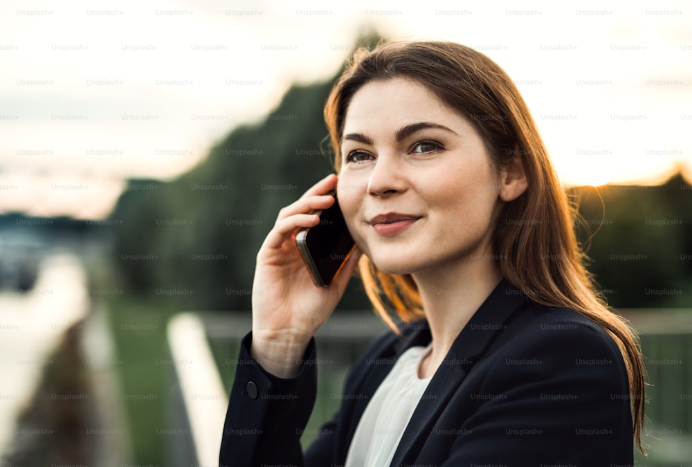 A close-up of a young businesswoman with smartphone outdoors, making a phone call.