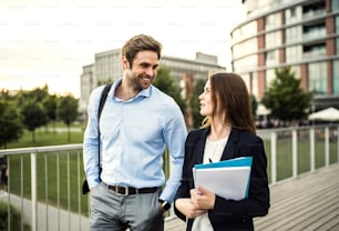 A young businessman and businesswoman walking on a bridge, talking.