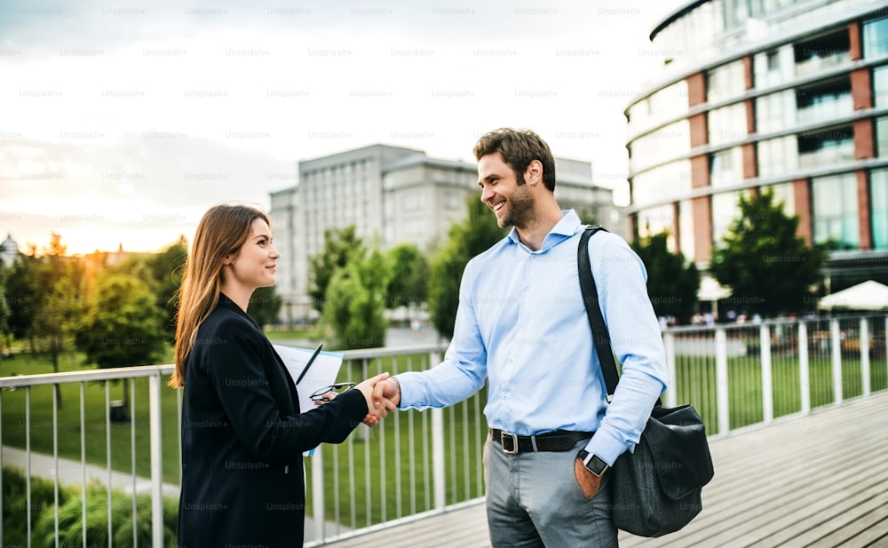 Young businessman and businesswoman standing on the bridge, shaking hands.