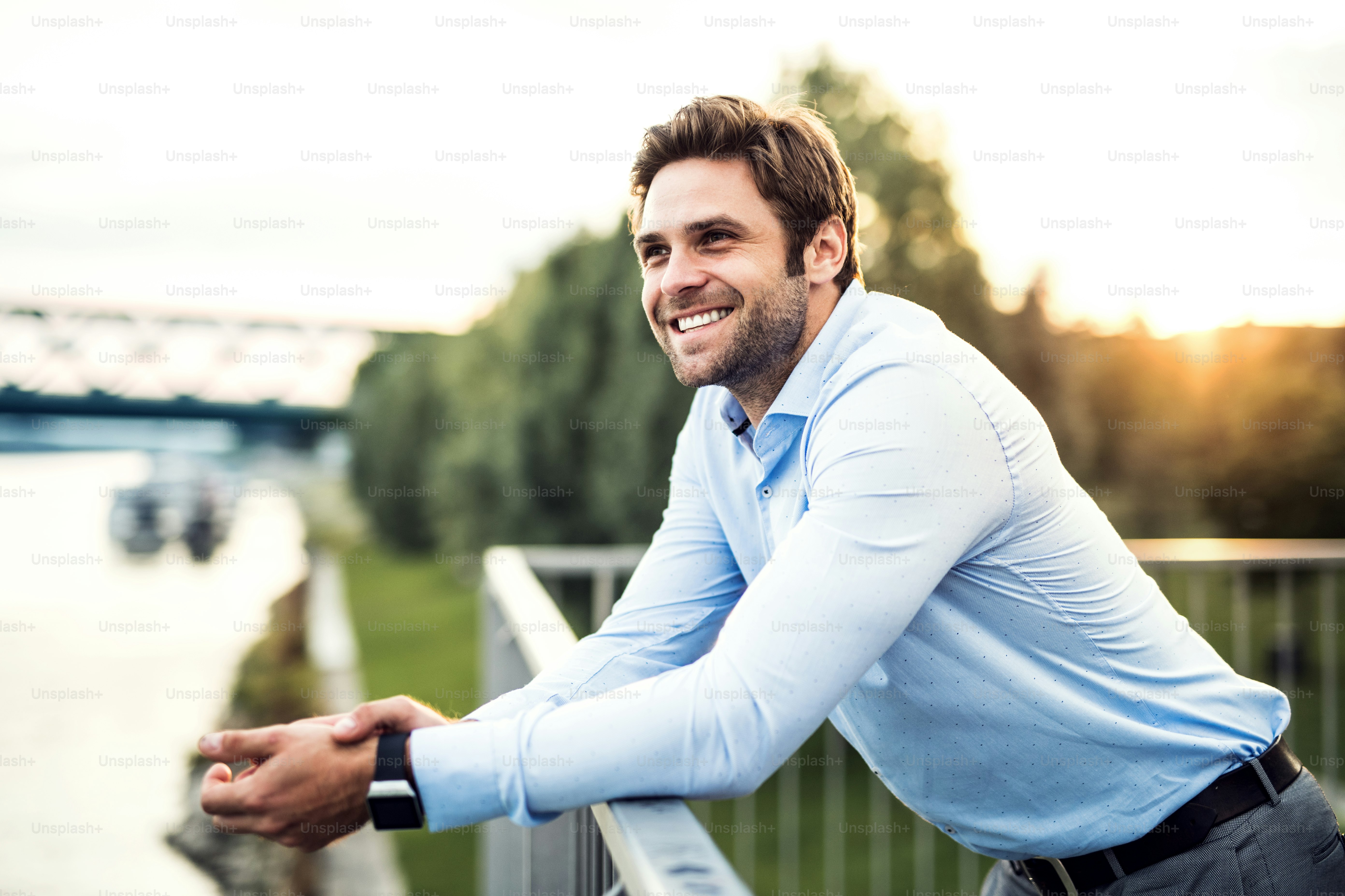 A young businessman standing on a bridge, leaning on a railing. Copy space.