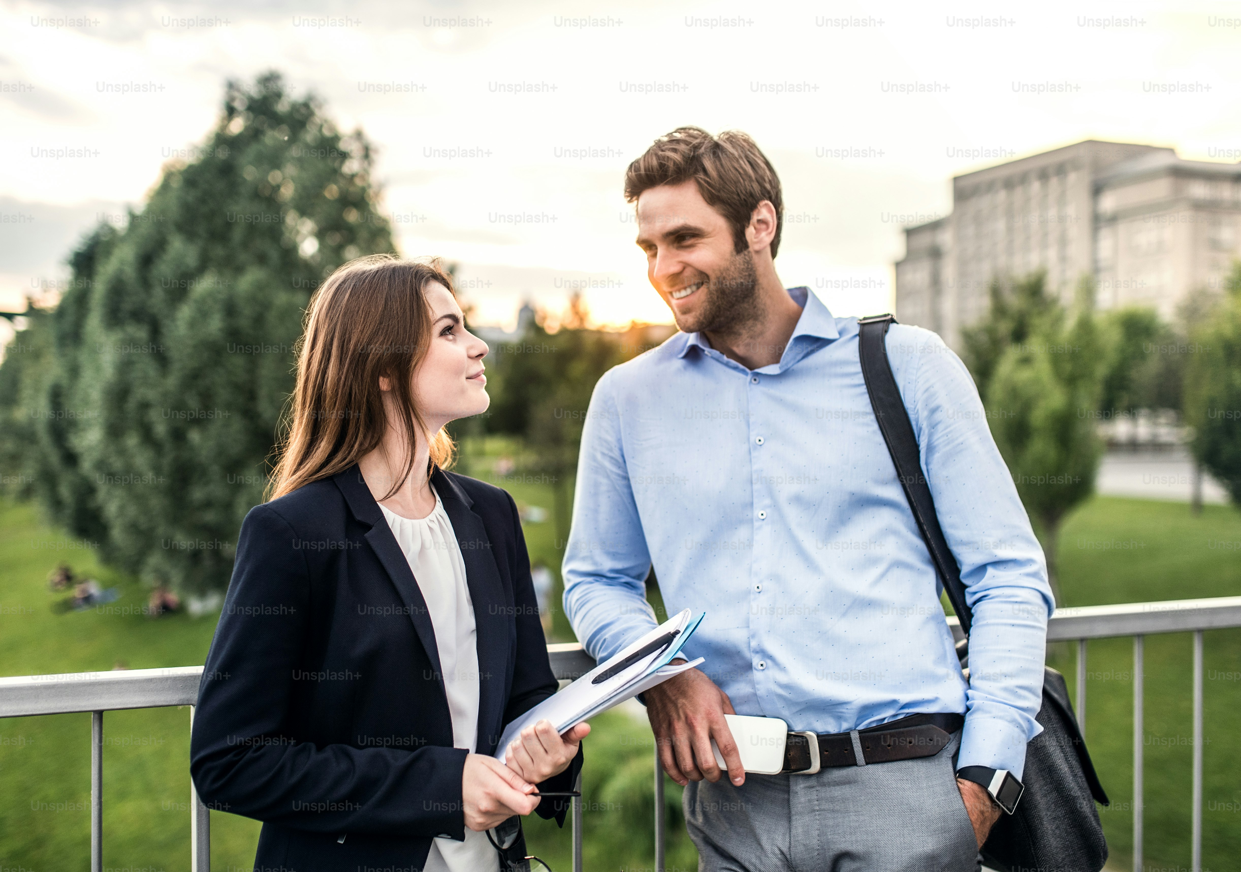 Ein junger Geschäftsmann und eine Geschäftsfrau stehen auf einer Brücke und unterhalten sich.