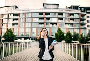 Uma jovem empresária feliz com óculos e smartphone andando na ponte de uma cidade, fazendo um telefonema.