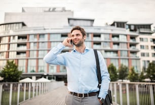 A young businessman with a smartphone walking on a bridge, making a phone call.