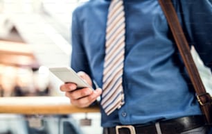 Un joven hombre de negocios irreconocible con un teléfono inteligente caminando en un edificio moderno, mensajes de texto. Espacio de copia.