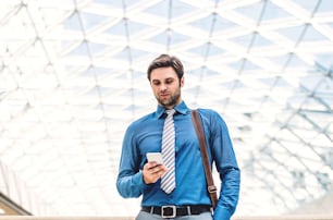 A young businessman with smartphone walking in a modern building, text messaging. Copy space.