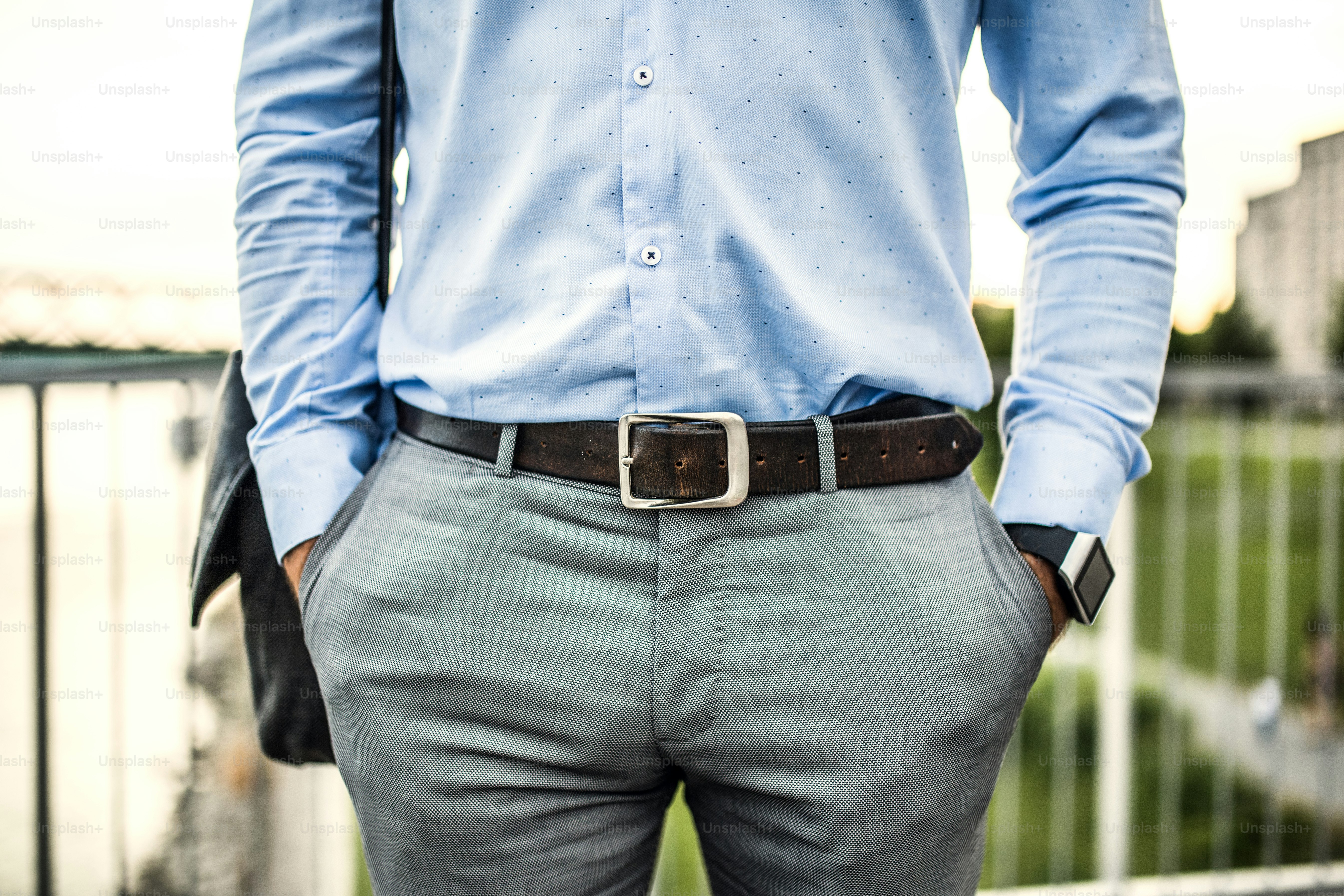 An unrecognizable young businessman with a bag and a leather belt walking on a bridge, hands in pockets.