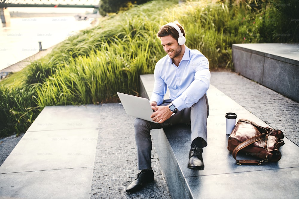 Um homem de negócios com smartwatch, laptop e fones de ouvido, sentado ao ar livre em escadas de concreto.
