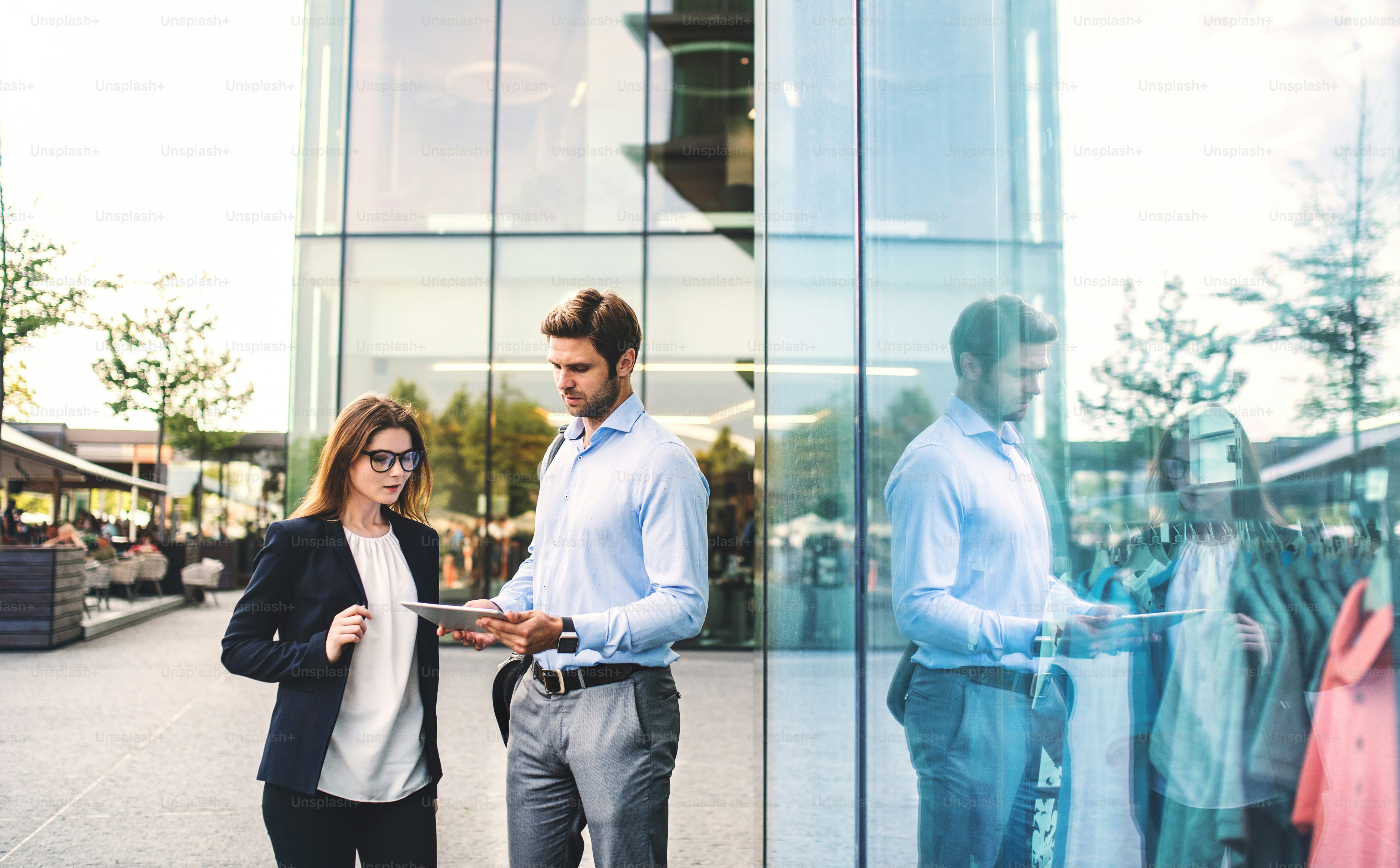 A young businessman and businesswoman standing on the street outdoors, using tablet