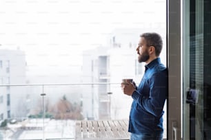 Ein Mann, der am Fenster steht und zu Hause eine Tasse Kaffee in der Hand hält.