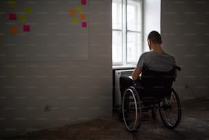 Un homme en fauteuil roulant regardant par la fenêtre. Vue arrière.