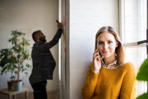Dos empresarios en la oficina trabajando juntos. Una mujer con teléfono inteligente, haciendo una llamada telefónica.