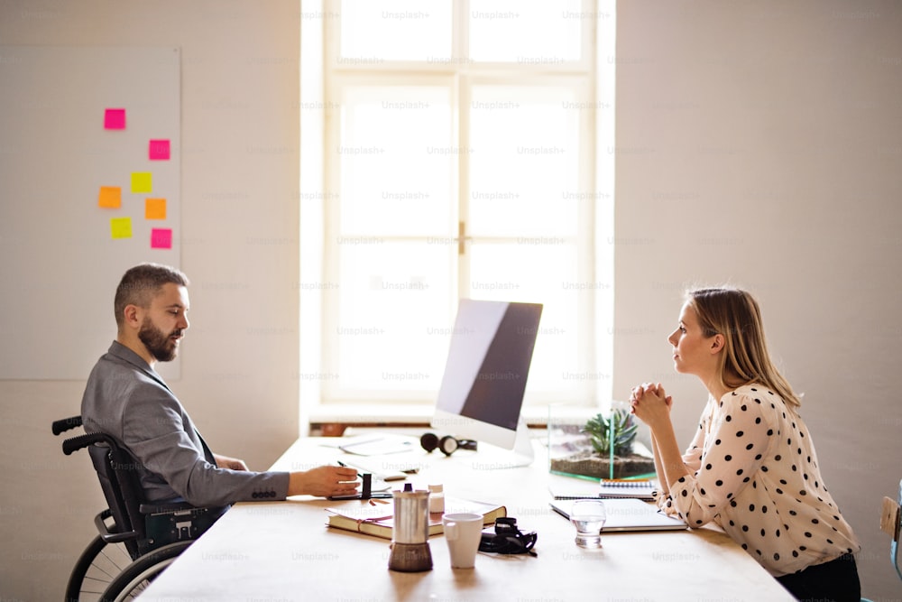 Two business people with wheelchair in the office working together.