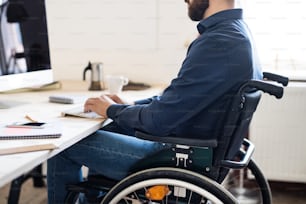 Homme d’affaires méconnaissable en fauteuil roulant travaillant au bureau.