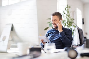 Geschäftsmann im Rollstuhl mit Smartphone am Schreibtisch im Büro, telefonierend.