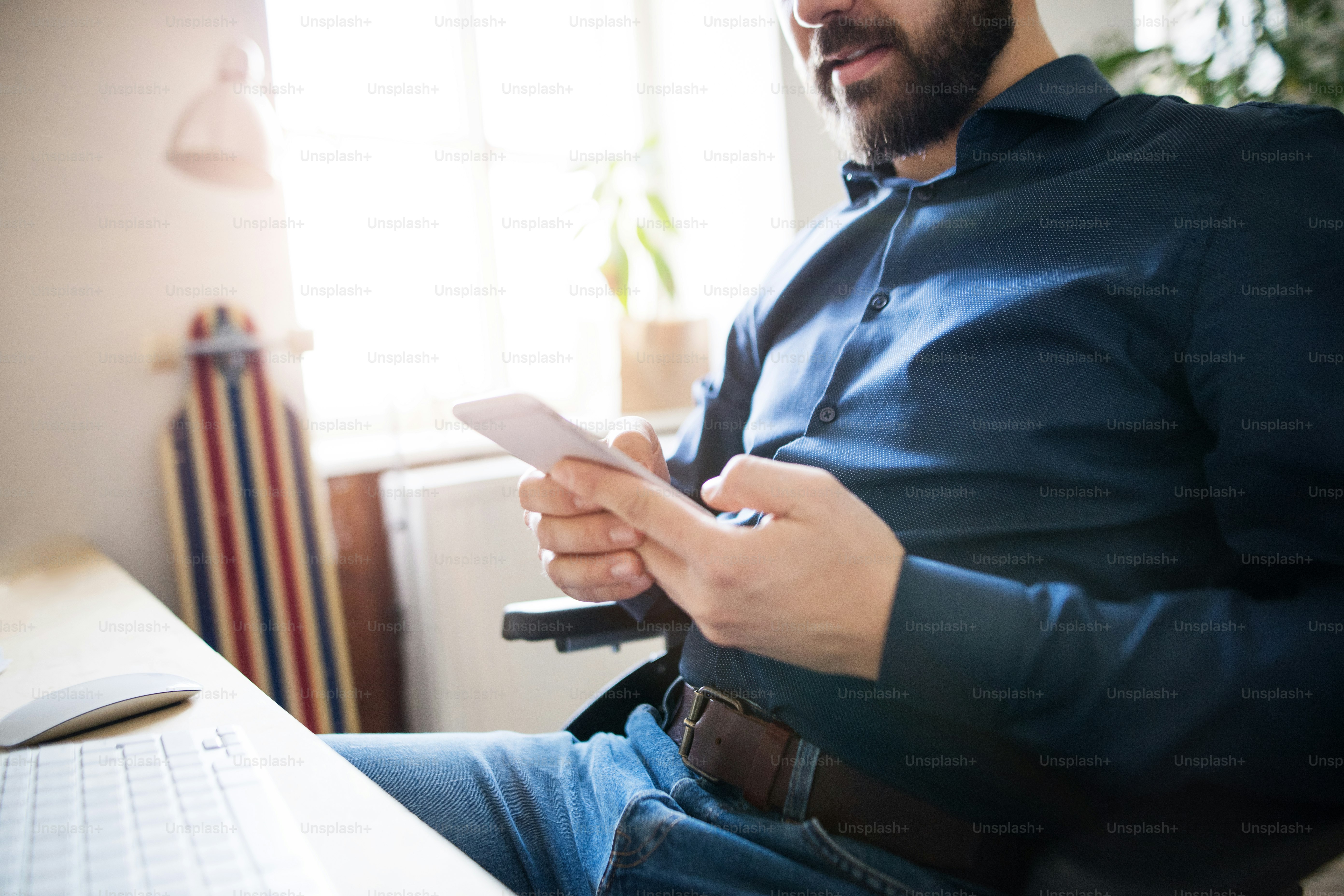 Unkenntlicher Geschäftsmann im Rollstuhl mit Smartphone am Schreibtisch im Büro, SMS.