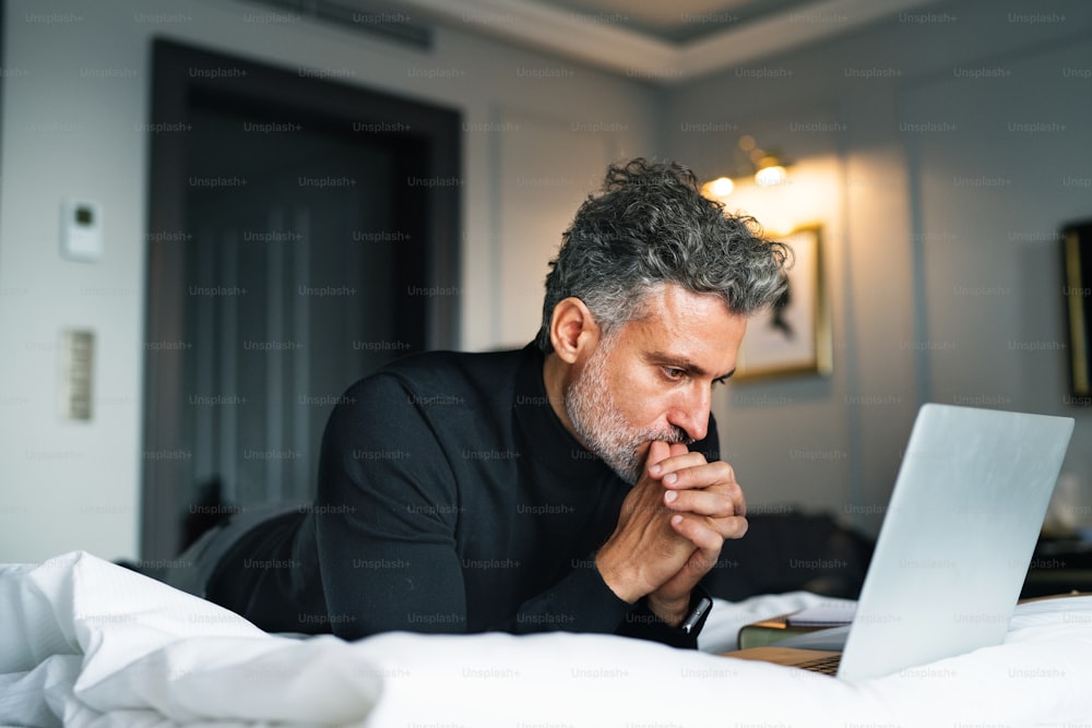 Hombre de negocios maduro con computadora portátil en una habitación de hotel. Hombre guapo trabajando en la computadora.