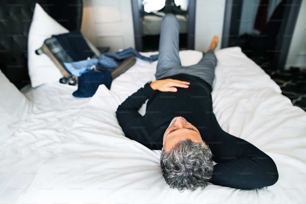 Hombre de negocios maduro en una habitación de hotel. Hombre guapo acostado en una cama, descansando.